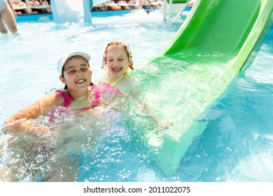 Two Girls Splash In An Outdoors Swimming Pool In Summer. Happy Children, Sister Playing, Enjoying Sunny Weather In Public Pool