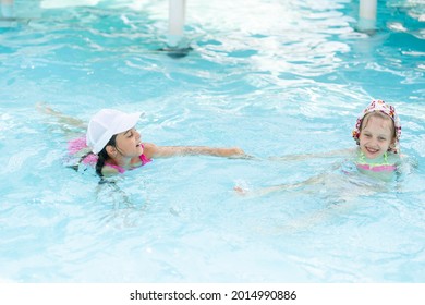 Two Girls Splash In An Outdoors Swimming Pool In Summer. Happy Children, Sister Playing, Enjoying Sunny Weather In Public Pool