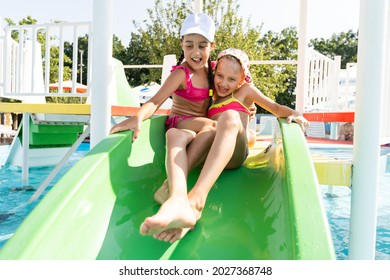 Two Girls Splash In An Outdoors Swimming Pool In Summer. Happy Children, Sister Playing, Enjoying Sunny Weather In Public Pool