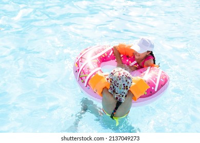 Two Girls Splash In An Outdoors Swimming Pool In Summer. Happy Children, Sister Playing, Enjoying Sunny Weather In Public Pool