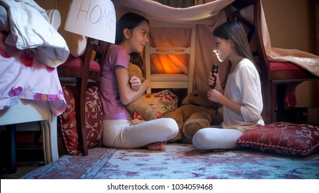 Two Girls Telling Stories With Flashlight In Selfmade Tent