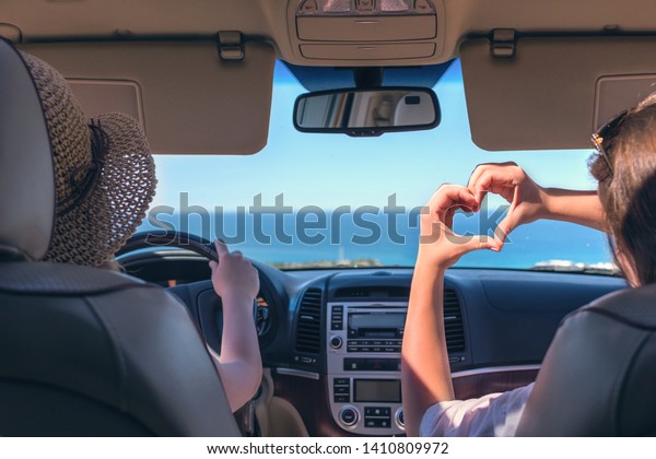 Two girls traveling by car on the\
Italy. One of them  holds her hands in the form of heart\
