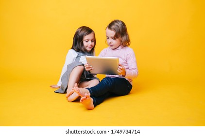 Two girls use a digital tablet on an isolated yellow background with copy space - Powered by Shutterstock