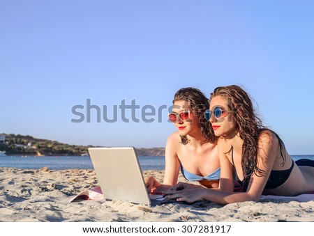 Two girls using a laptop at the beach