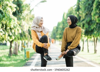 two girls in veil stretching their leg muscles by lifting and holding the bent leg with their arms before jogging in the park - Powered by Shutterstock