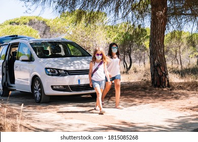 Two Girls Walking With Bright Sunglasses And Face Mask After A Stop On The Summer Vacation Road Trip In The Middle Of The Covid19 Coronavirus Pandemic On A Sandy Pine Road