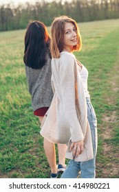 Two Girls Walking Outdoors At Sunset. One Girl Has Turn Around. Best Friends