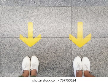 Two girls wear same white sneakers standing in front of yellow arrows, waiting at subway. direction, similarity, team power concept 