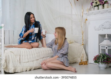 two girls,sisters and friends,blond and brunette sitting and drinking tea, talking at home and smiling
