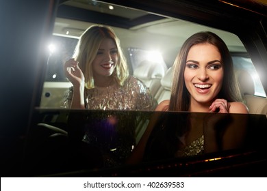 Two glamorous women laughing in the back of a limousine