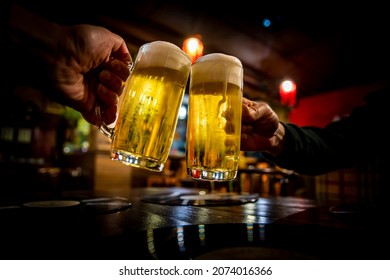 two glass of beer in hand. Beer glasses clinking in bar or pub - Shutterstock ID 2074016366