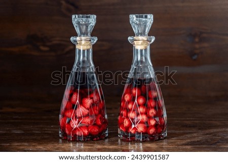 Two glass bottles of homemade cherry and raspberry liqueur on a wooden background, close up. Berry alcoholic drinks concept