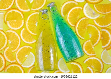 Two glass bottles on a bright tropical citrus background. Blue and yellow drinks with seeds. Orange slices, fruit smoothie. Beverage in water. Summer lemonade with drops. Soft drink, juice. Thirst. - Shutterstock ID 1938626122