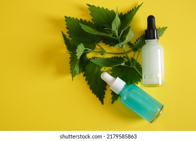 Two Glass dropper bottles of nettle oil or serum and nettle leaves on bright yellow background top view opy space nettle benefits for skin, natural cosmetics concept