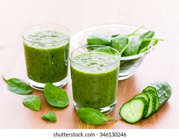 Two glass of green smoothie with spinach and cucumber on wooden surface