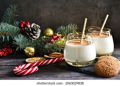 Two glass homemade winter eggnog with cinnamon, and fir tree branches, cookies, sweet candy on wooden table. Traditional Christmas dessert - Powered by Shutterstock