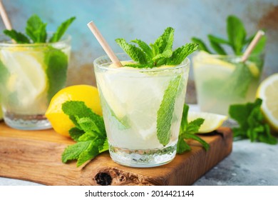 Two glass with lemonade or mojito cocktail with lemon and mint, cold refreshing drink or beverage with ice on rustic blue background.