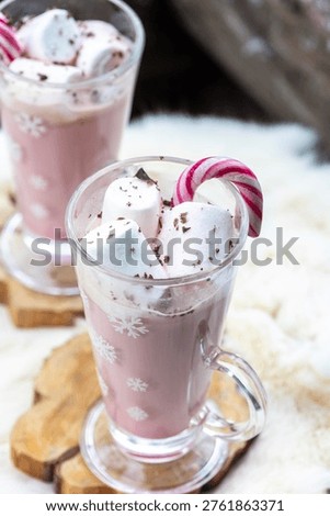 Two glass mugs filled with ruby chocolate hot chocolate topped with whipped cream, marshmallows and a candy cane. The snowflake mugs, wooden coasters and soft fur surface create a cozy, festive winter atmosphere with a distinctive pink ruby chocolate tone.