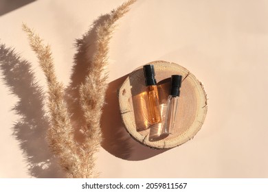 Two Glass Perfume Samples On A Wooden Tray Lying On A Beige Background With Pampas Grass. Luxury And Natural Cosmetics Presentation. Testers On A Woodcut In The Sunlight. Top View