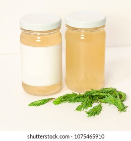 Two Glass Product Jars With Fresh Fir Tips Against A White Background.