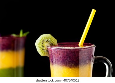 Two Glass Of Smoothie With Colorful Layers From Kiwi, Oranges And Blackberry On Black Background Close Up