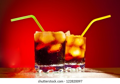 two glass transparent glass with ice cubes and Coke with a green tube on blue background Space for inscriptions