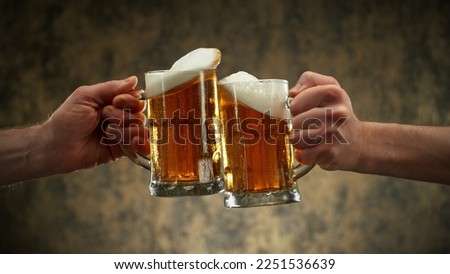 Two glasses of beer in cheers gesture, splashing out. Isolated on shabby background.