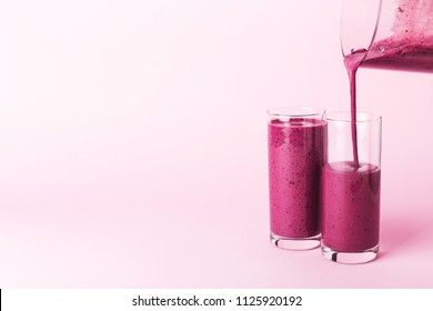 Two glasses of blueberries smoothie on pink background. Poring from blender into glass. - Powered by Shutterstock