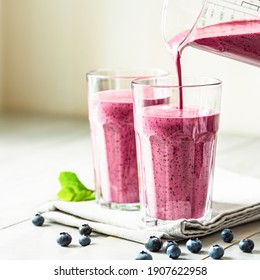 Two glasses of blueberry smoothie with mint garnish and straw on the table. Berry shake is poured into a glass. - Powered by Shutterstock