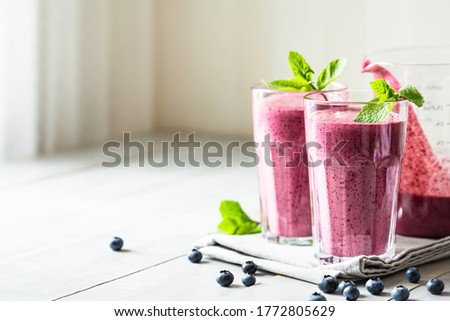 Two glasses of blueberry smoothie with mint garnish on the table.