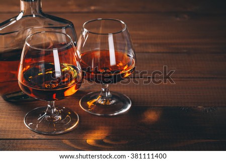 Two glasses of brandy or cognac and bottle on the wooden table.