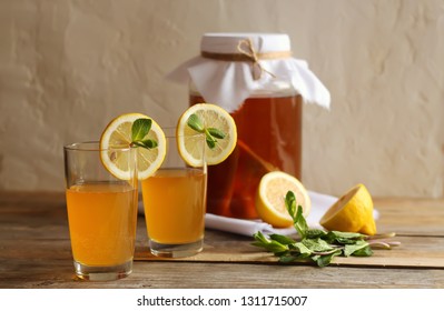 Two Glasses And A Can Of Homemade Kombucha Tea With Lemon Slices And Mint. Wooden Table, Light Background, Rustic. Copy Space, Horizontal Orientation