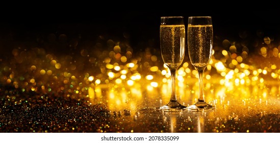 Two glasses of champagne on the background of bokeh and glitter lights, new year 2022