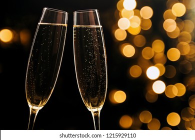 Two glasses of champagne on black stylish background with golden bokeh circles. Place for text. Festive concept.