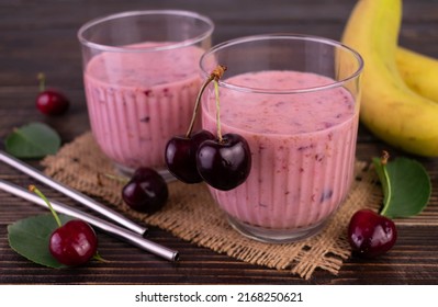 Two Glasses Of Cherry And Banana Smoothie On A Dark Wooden Background.
