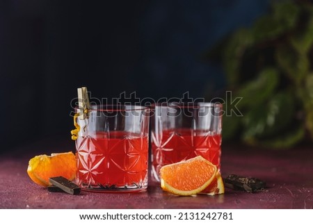 Two glasses of chocolate red orange negroni, an italian cocktail, an aperitif, first mixed in Firenze, Italy, in 1919, alcoholic bitter cocktail served by ingredients on the dark claret table.