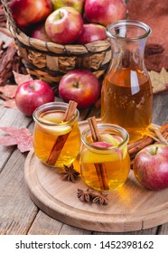 Two glasses of cider with apple slices and cinnamon on a wooden platter