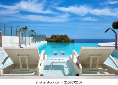 Two Glasses With Cocktails On Table Between Deck Chairs Sunbeds On Swimming Pool, Sea, Blue Sky Background On Poolside. Summer Holidays, Relax, Accommodation In Luxury Hotel Concept, No People. Spain