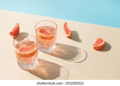 Two glasses of drink with slices of fresh grapefruit against bright beige and blue background. Creative minimal summer concept. Sunny day shadows.