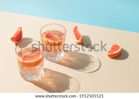 Two glasses of drink with slices of fresh grapefruit against bright beige and blue background. Creative minimal summer concept. Sunny day shadows.