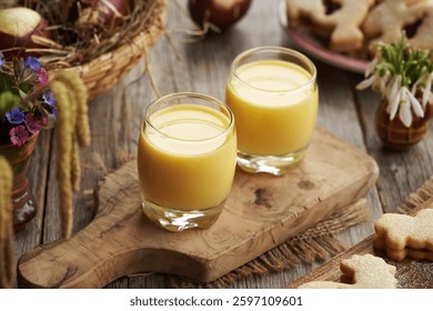 Two glasses of Eiecognac with dyed Easter eggs and spring decoration on a wooden table