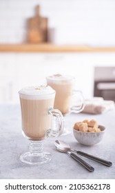 Two glasses of fragrant cappuccino coffee with cinnamon and brown sugar on a blue table against the background of a white kitchen in the early morning. Breakfast concept. Front view.