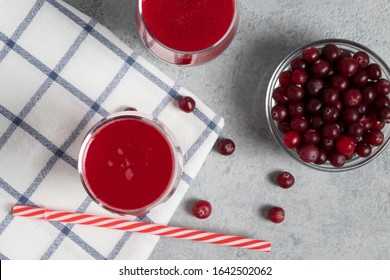 Two Glasses With Homemade Freshly Cranberry Juice And A Bowl Of Cranberries On A Gray Concrete Table, Top View, Flat Lay