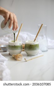 Two Glasses With Ice Matcha Oat Milk Latte And Bamboo Straws. Woman Hand Making It. Matcha Set  Tools Made Of  Bamboo In The Background. Healthy Vegan Antioxidant Drink Concept. Copy Space 