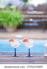 Two glasses with ice and a slice of grapefruit on a table by a pool