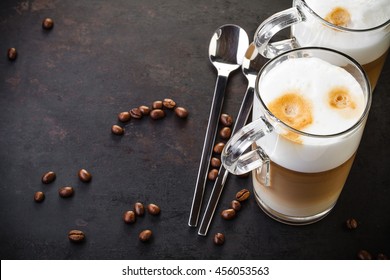 Two Glasses Of Latte Ad Spoons On Dark Rustic Background