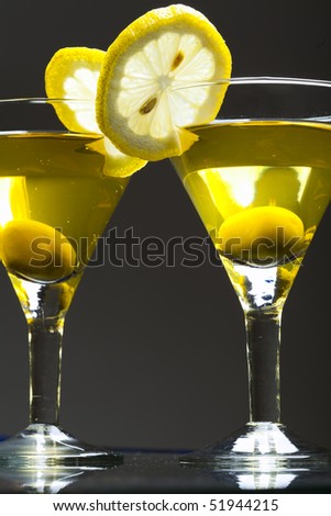 Two glasses  of martini with olive and lemon on black background