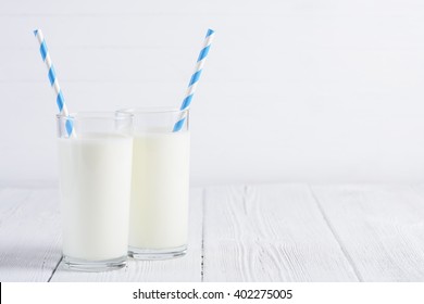 Two glasses of milk with blue stripped paper straws on wooden table still life - Powered by Shutterstock