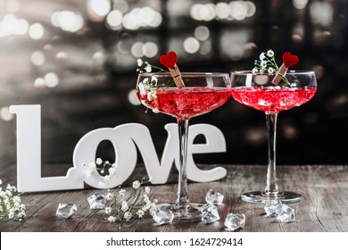 Two glasses with pink champagne wine and wooden word LOVE on a bar counter. Celebration Valentines day, greeting card. Black, white and red color cheme