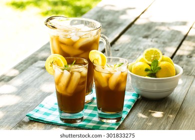 Two Glasses And Pitcher Of Iced Tea With Lemons On Picnic Table